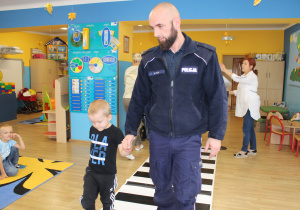 Oluś z funkcjonariuszem Policji podczas ćwiczeń przechodzenia przez jezdnię (ćwiczenia w sali)