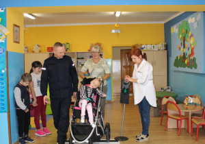 Marika z panią Elą i funkcjonariuszem Policji podczas ćwiczeń przechodzenia przez jezdnię (ćwiczenia w sali)
