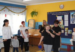 Natalia pod opieką p. Moniki recytuje wierszyk, w tle pozostałe przedszkolaki i panie