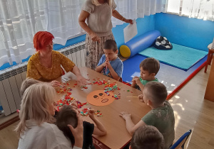 Dzieci z grupy 3 rozdmuchują przez słomki bibułę z emotki przedstawiającej strach.