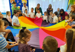 Przedszkolaki z paniami i laureatami konkursu biorą udział w zabawie z chustą animacyjną