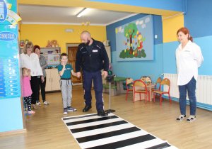 Adaś z funkcjonariuszem Policji podczas ćwiczeń przechodzenia przez jezdnię (ćwiczenia w sali)