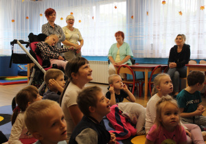 Przedszkolaki Miłosz, Lena, Maja, Olek, Denisa, Adaś, Marika, Hana i Karol siedzą na dywanie, w tle panie - Ania K., Ania Sz., Ela i Basia