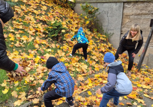 Jesienne zabawy na świeżym powietrzu - na zdjęciu przedszkolaki wraz z paniami obrzucają się liśćmi