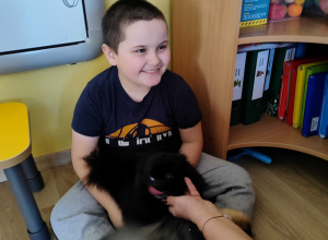 Zajęcia z dogoterapii - Mikołaj przytula małego pieska.