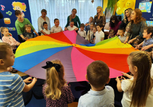 Przedszkolaki z paniami i laureatami konkursu biorą udział w zabawie z chustą animacyjną