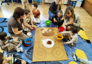 Dzieci wyklejają misia różnymi materiałami.