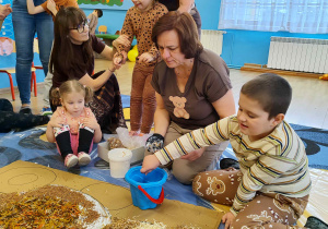 Dzieci wyklejają misia różnymi materiałami.