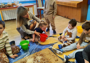 Dzieci wyklejają misia różnymi materiałami.