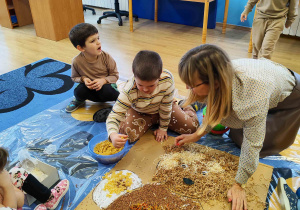 Dzieci wyklejają misia różnymi materiałami.