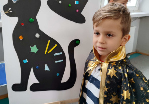 Boguś prezentuje ozdobionego czarnego kota i kapelusz.