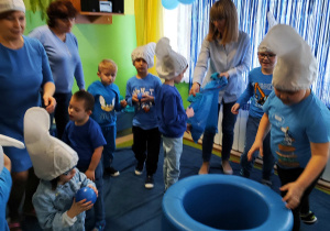 Dzień niebieski - dzieci wrzucają piłki i woreczki do niebieskiej beczki.