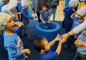 Dzień niebieski - dzieci wrzucają piłki i woreczki do niebieskiej beczki.