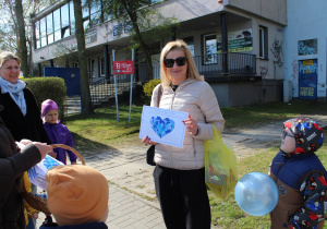 Przedszkolne obchody Dni Autyzmu - na zdjęciu przedszkolaki wręczają niebieskie serduszka przechodniom