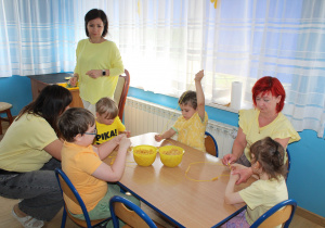 Żółty dzień w przedszkolu - Yaroslav, Bohdan, Mikołaj i Nadia z pomocą p. Ani i Oksany robią makaronowe korale, w tle p. Paulina
